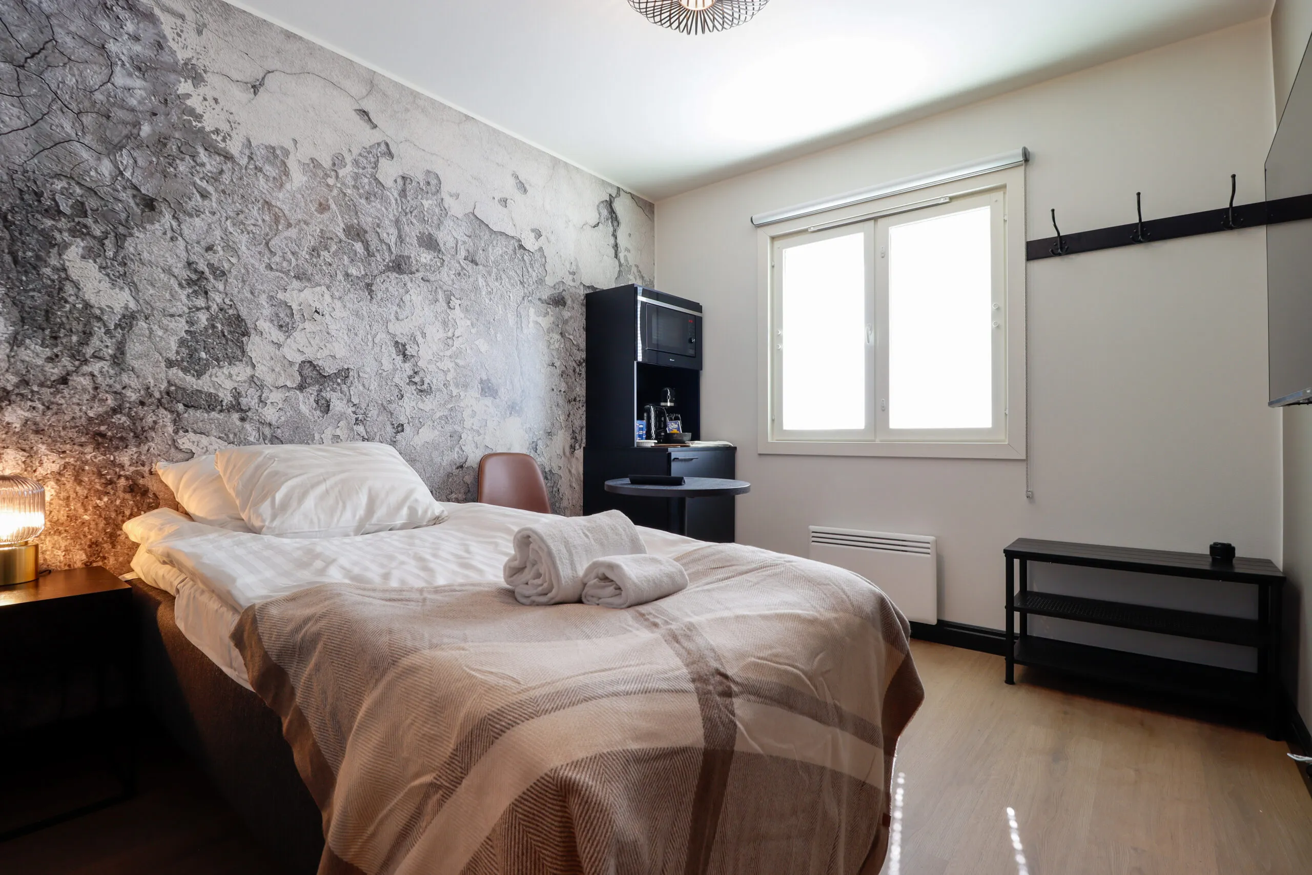 Hotellihuoneen sänky ja betonipintainen tehosteseinä